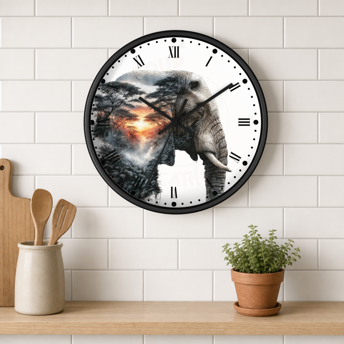 A round wall clock with a black frame hangs on a white subway-tile wall above a wooden shelf. The clock face features a white background with black Roman numerals and a central graphic of an elephant overlaid with a dramatic sunset landscape scene.