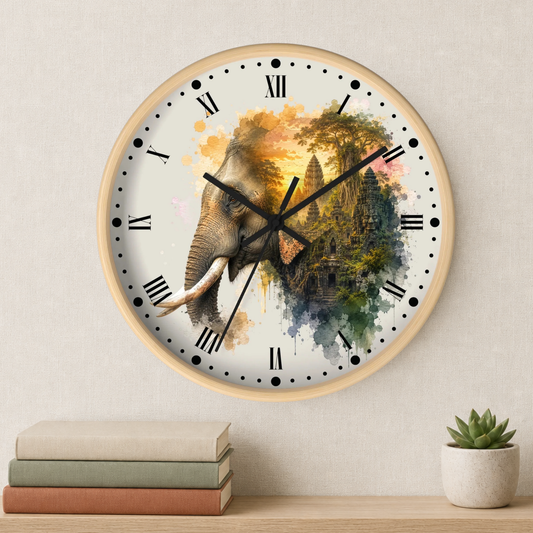 A round wall clock with a light wood frame hangs on a beige wall above a shelf with stacked books and a small potted succulent. The clock face features a watercolor-style elephant merging into a temple scene with gold, green, blue, and pink tones, black Roman numerals, and black hands.