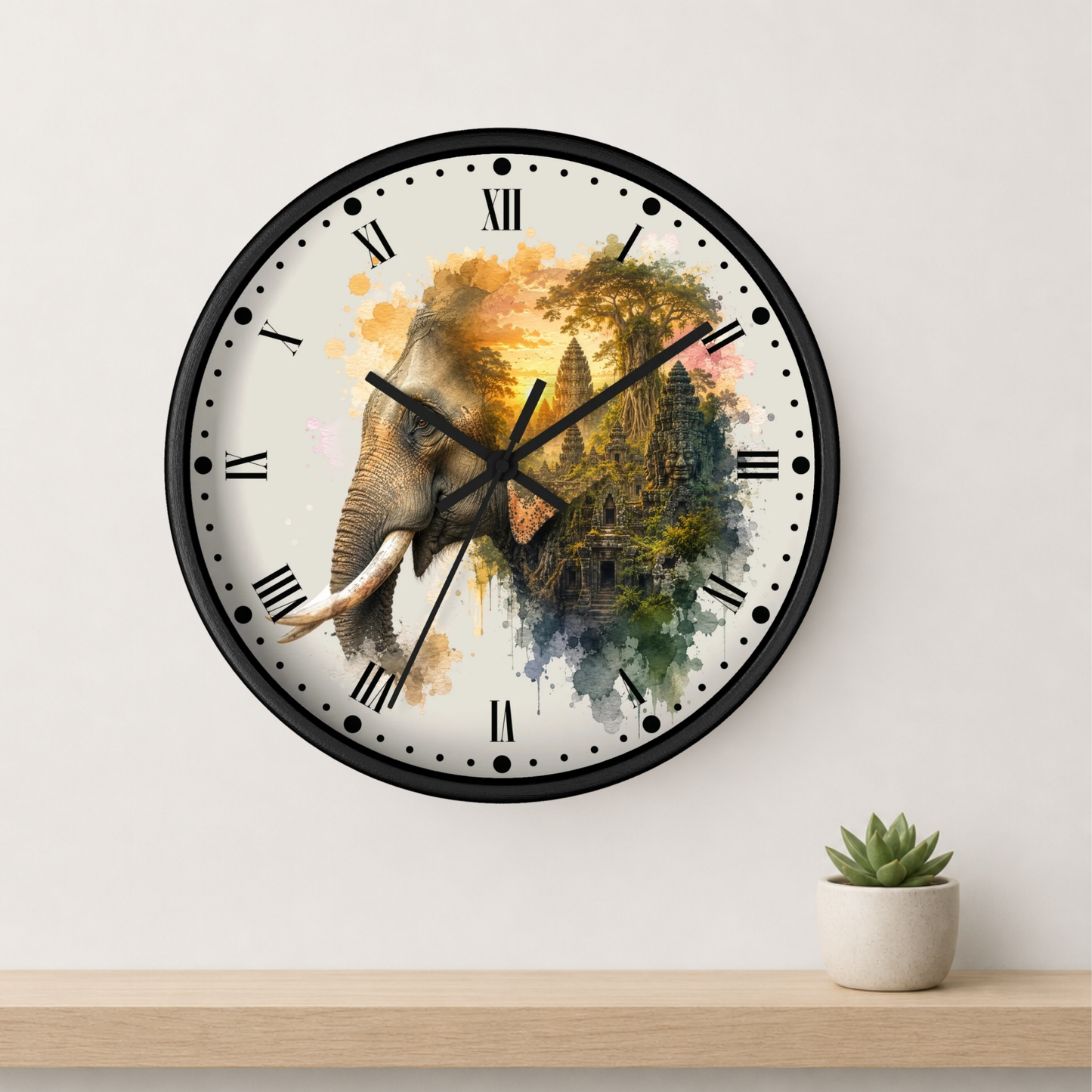 A round wall clock with a black frame and a watercolor-style elephant design on the face, mounted on a light wall above a wooden shelf with a small potted succulent.