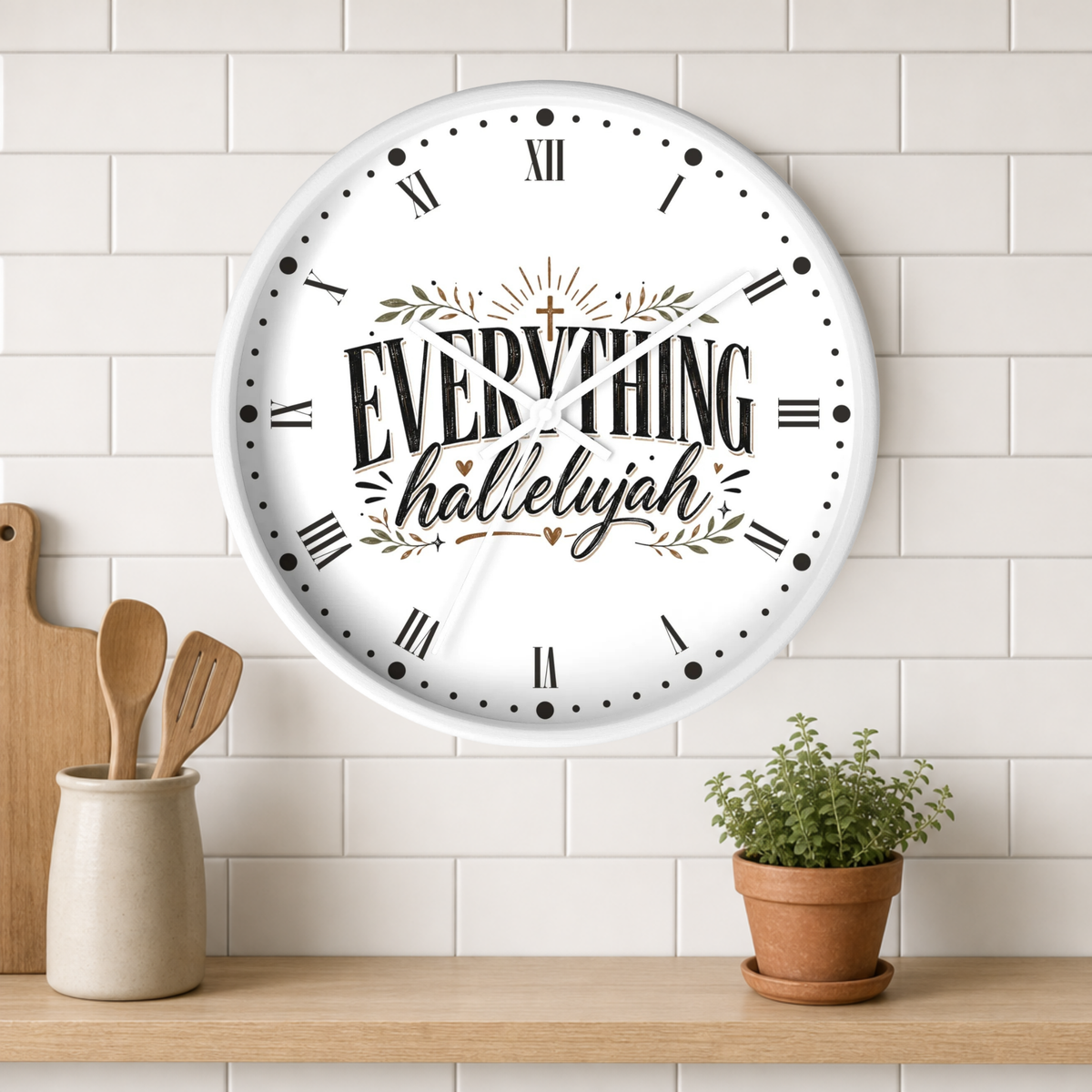A round white wall clock with black Roman numerals and the words “EVERYTHING halleyyah” in decorative script, mounted on a white subway tile wall above a wooden shelf with kitchen utensils and a potted plant.
