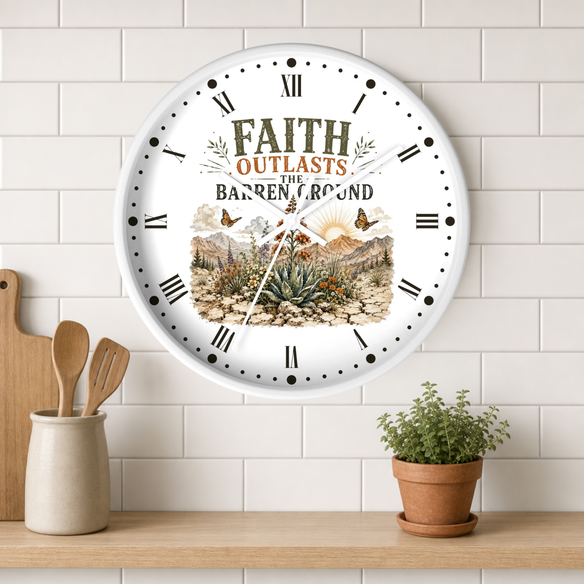 A round white wall clock with Roman numerals and a scenic desert landscape illustration, featuring the text 'FAITH OUTLASTS THE BARREN LAND.' The clock is mounted on a white subway tile wall above a wooden shelf with a small potted plant and wooden utensils.