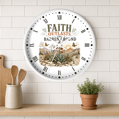A round white wall clock with Roman numerals and a scenic desert landscape illustration, featuring the text 'FAITH OUTLASTS THE BARREN LAND.' The clock is mounted on a white subway tile wall above a wooden shelf with a small potted plant and wooden utensils.