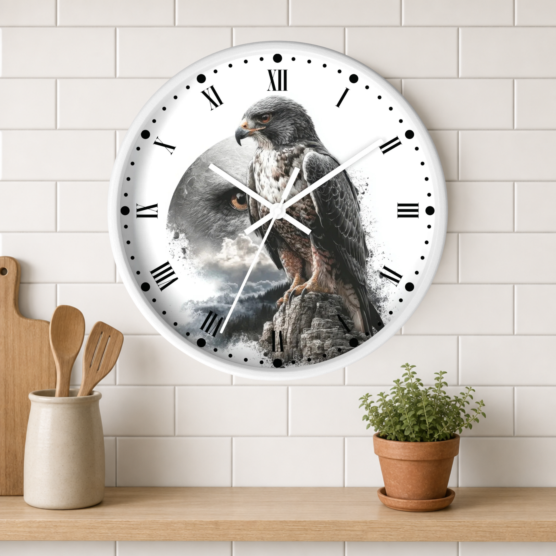 A round wall clock with a white frame and Roman numerals, featuring a printed design of a large bird of prey perched on a rock against a stormy sky. The clock is mounted on a white subway-tile wall above a wooden shelf with kitchen utensils and a small potted plant.
