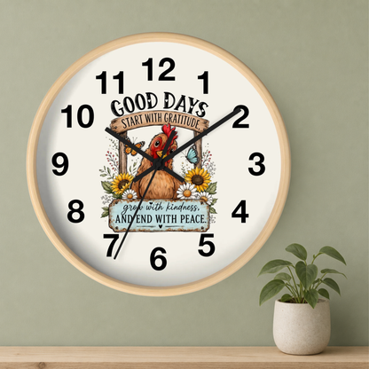 A round wall clock with a light wood frame and a white face, featuring a chicken illustration and the text 'GOOD DAYS START WITH GRATITUDE' and 'grow with kindness, AND END WITH PEACE.' The clock is mounted on a sage green wall above a wooden shelf with a small potted plant.