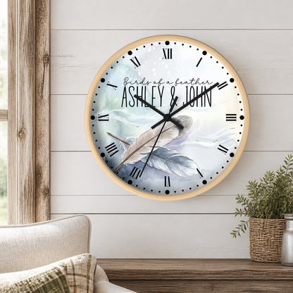 Round wood frame clock with a watercolor design of feathers on a blue background with the text "Birds of a feather and Ashely & John" mounted on a shiplap wall in a living room.