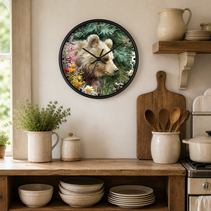 A round wall clock with a black frame hangs on a beige wall in a rustic kitchen setting. The clock face features a detailed illustration of a brown bear surrounded by colorful wildflowers and green foliage.