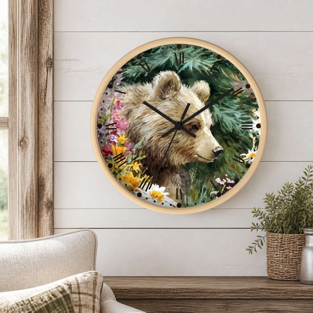 Round wall clock with a natural wood frame featuring a detailed illustration of a brown bear surrounded by green pine trees and colorful wildflowers. The clock is mounted on a white wood-paneled wall above a wooden shelf with a potted plant and a sofa visible in the foreground.