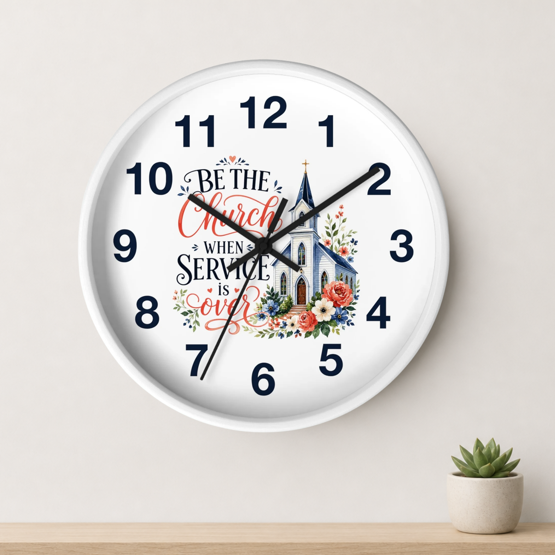 A round white wall clock with black numerals and hands, featuring a church illustration and the phrase 'Be the Church When Service is Over' in red and black script. The clock is mounted on a light beige wall above a wooden shelf with a small potted succulent.