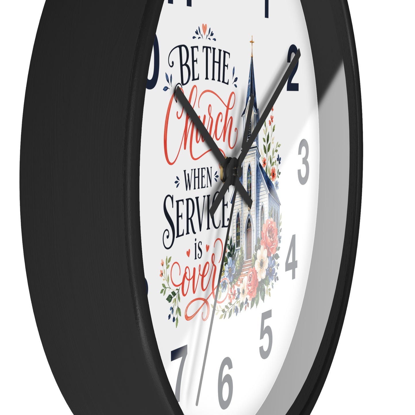 A close-up of a round wall clock with a black frame and a white face featuring the phrase 'Be the Church When Service is Over' in black and red script, alongside a church illustration and floral details.