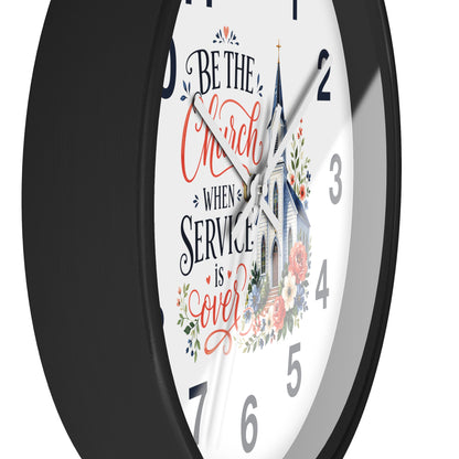A round wall clock with a black frame and a white face featuring the phrase 'Be the Church When Service is Over' in black and coral script, alongside an illustration of a church and floral details.