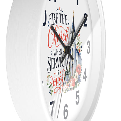 A white round wall clock with black hands and gray numerals, featuring a printed design on the face with the phrase 'Be the Church When Service is Over' in red and black script, a church illustration, and floral accents.