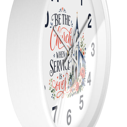 A white round wall clock with a printed church illustration and the phrase “Be the Church When Service is Over” in black and coral script, shown against a white background.
