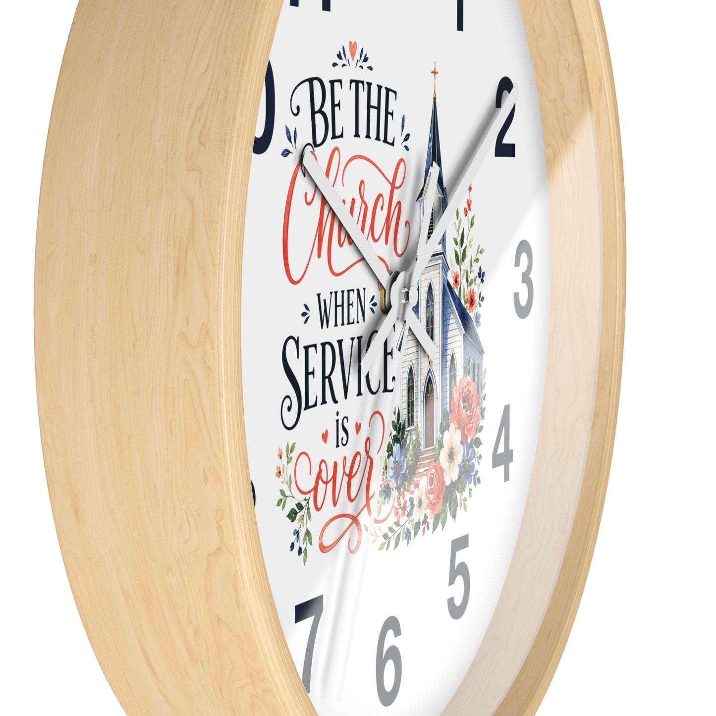 A close-up of a round wall clock with a light natural wood frame and a white face. The clock face features a church illustration and the hand-lettered quote, 'BE THE Church WHEN SERVICE is over' in black and coral-red script, with floral accents.