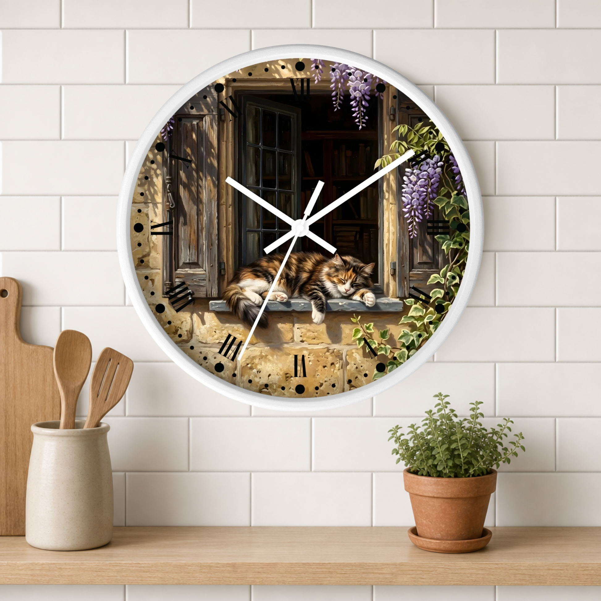 A round wall clock with a white frame hangs on a white subway-tile wall above a wooden shelf. The clock face features an illustration of a brown calico cat resting on a stone window sill, surrounded by purple wisteria flowers and green ivy.