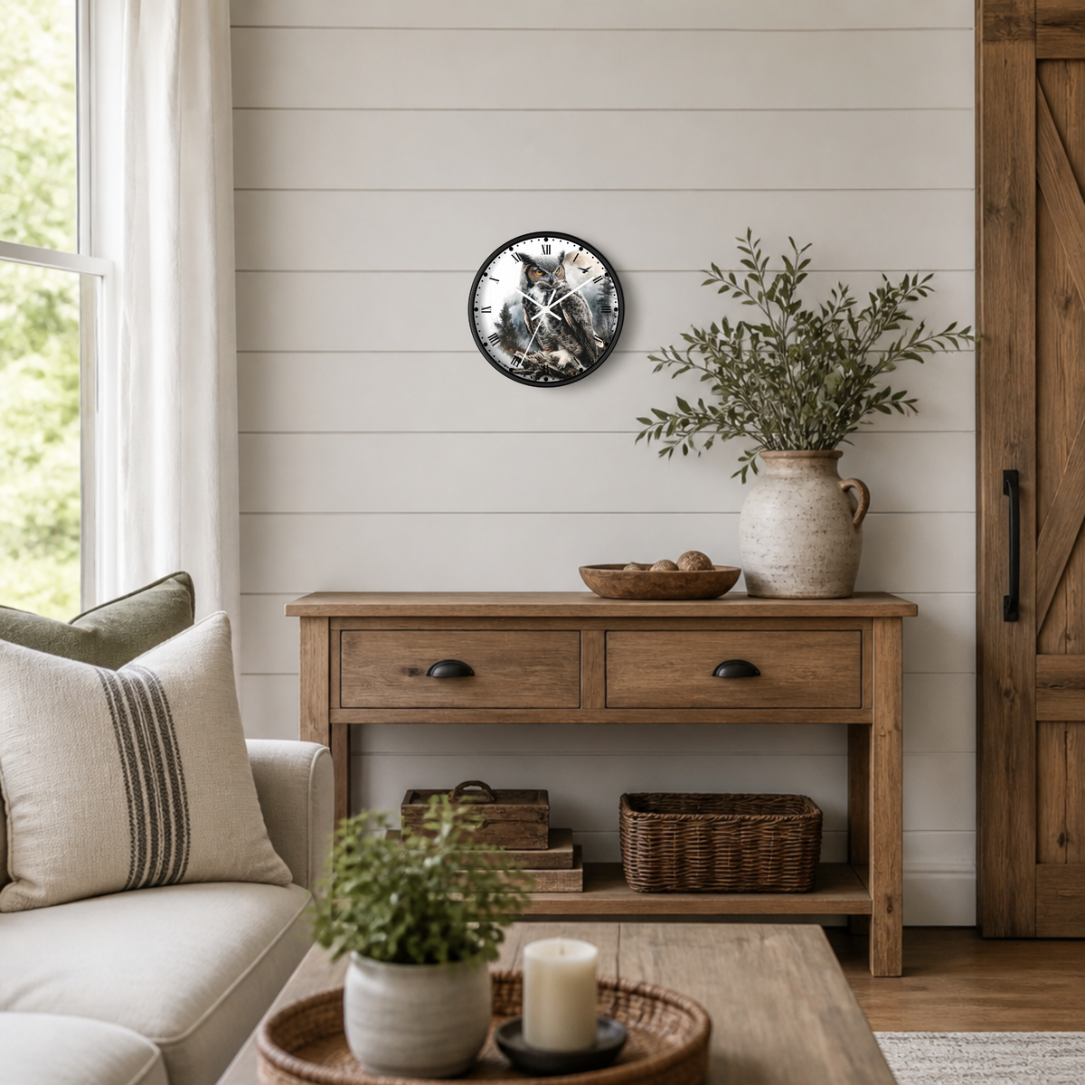 A round wall clock with a black frame and a rustic owl illustration, styled on a white shiplap wall above a wooden console table in a bright, modern farmhouse living room.