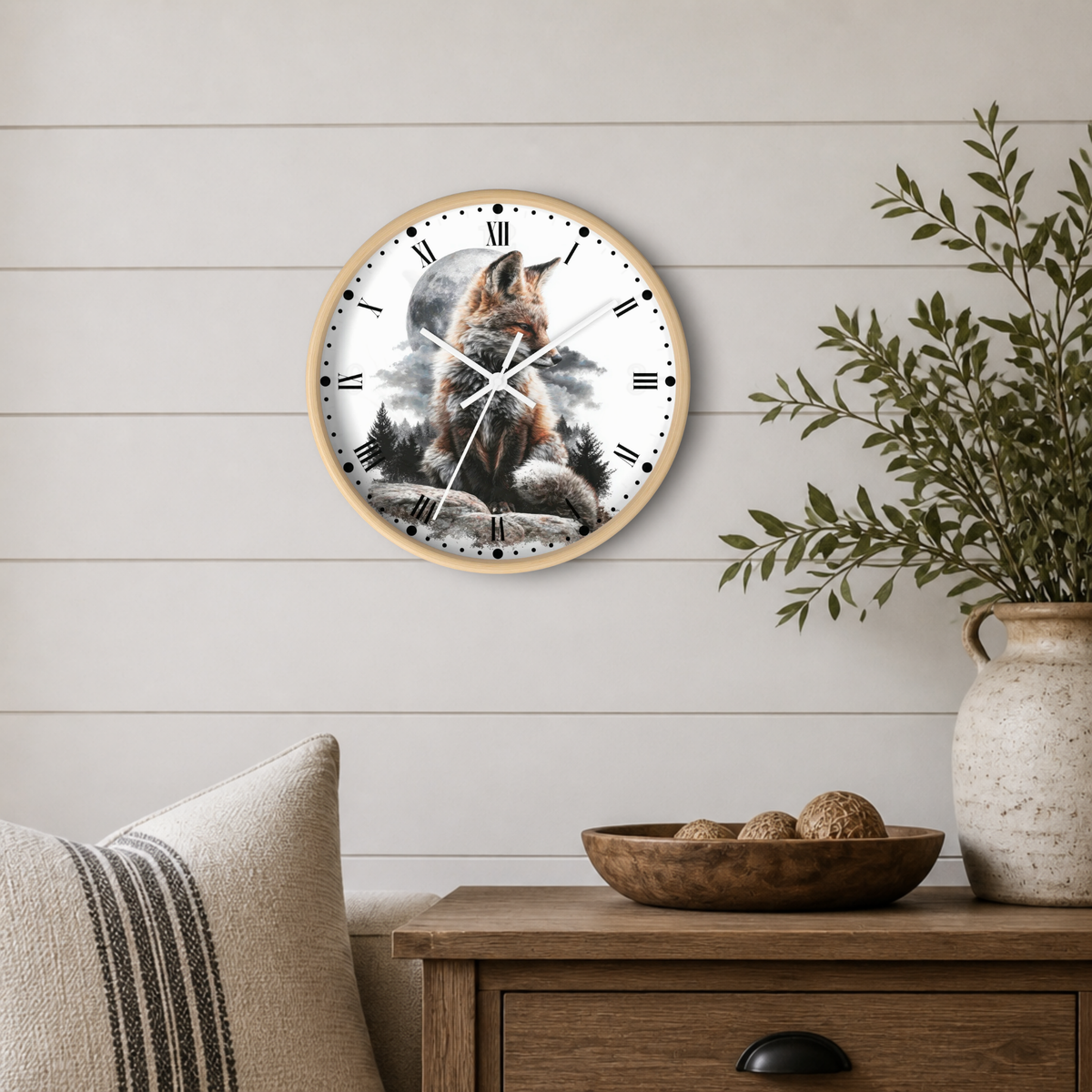 A round wall clock with a light wood frame hangs on a white shiplap wall above a wooden side table. The clock face features a detailed illustration of a fox sitting on rocks in front of a moonlit sky.