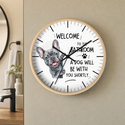A round wall clock with a light wood frame and a white face, featuring a French bulldog illustration and the text 'WELCOME TO THE BATHROOM A DOG WILL BE WITH YOU SHORTLY.