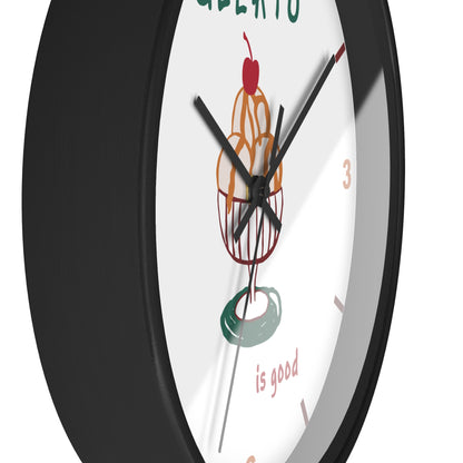 A close-up of a round wall clock with a black frame and a white face featuring a stylized illustration of a donut with a cherry and the words 'is good'.