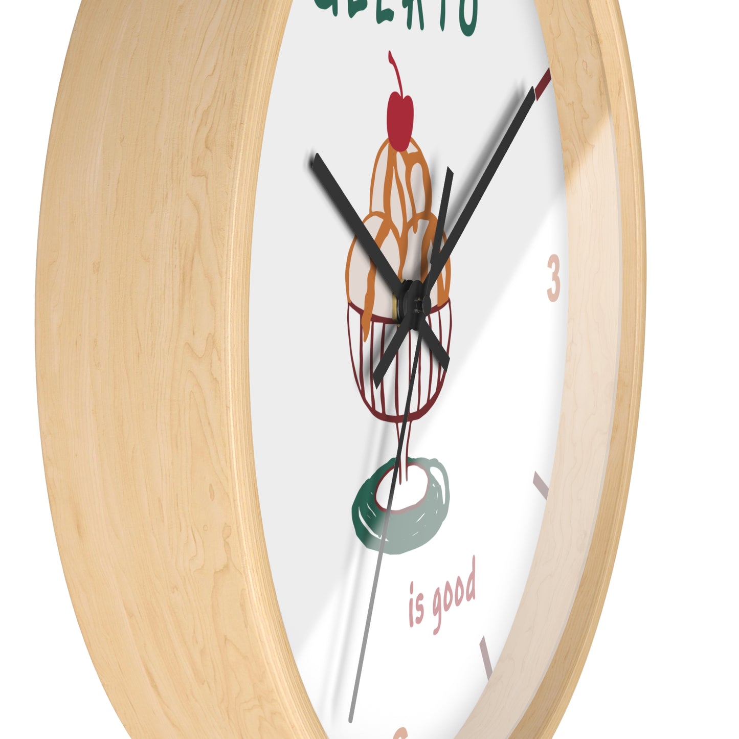 A close-up of a round wall clock with a light natural wood frame and a white dial featuring a colorful ice cream cone illustration and the words 'GELATO is good'.
