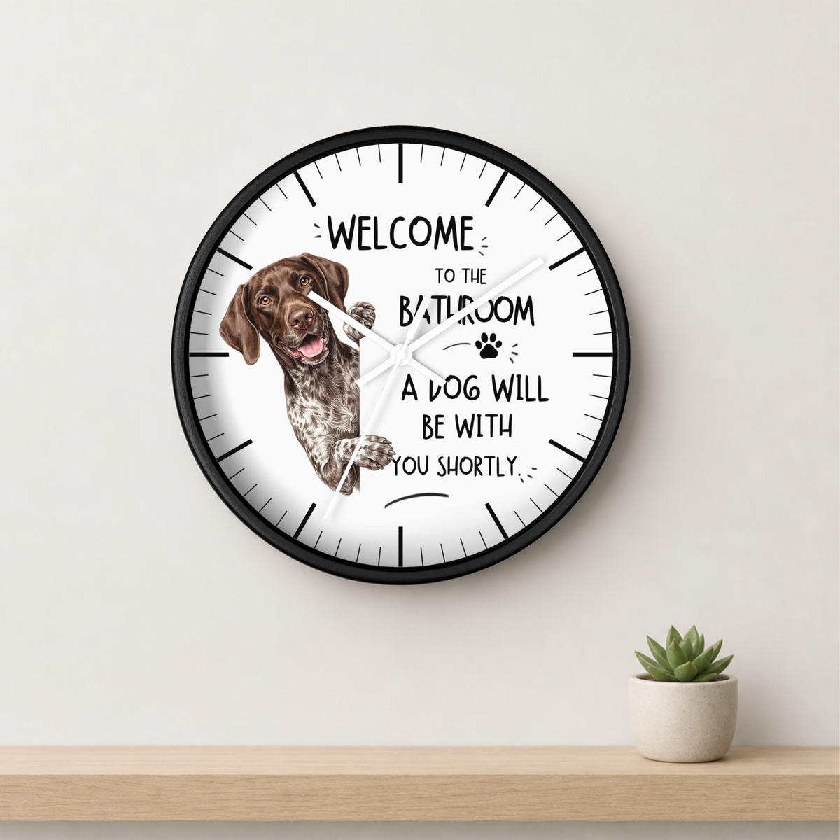 A round wall clock with a black frame and a white face, featuring a brown and white dog illustration and the text 'WELCOME TO THE BATHROOM A DOG WILL BE WITH YOU SHORTLY.
