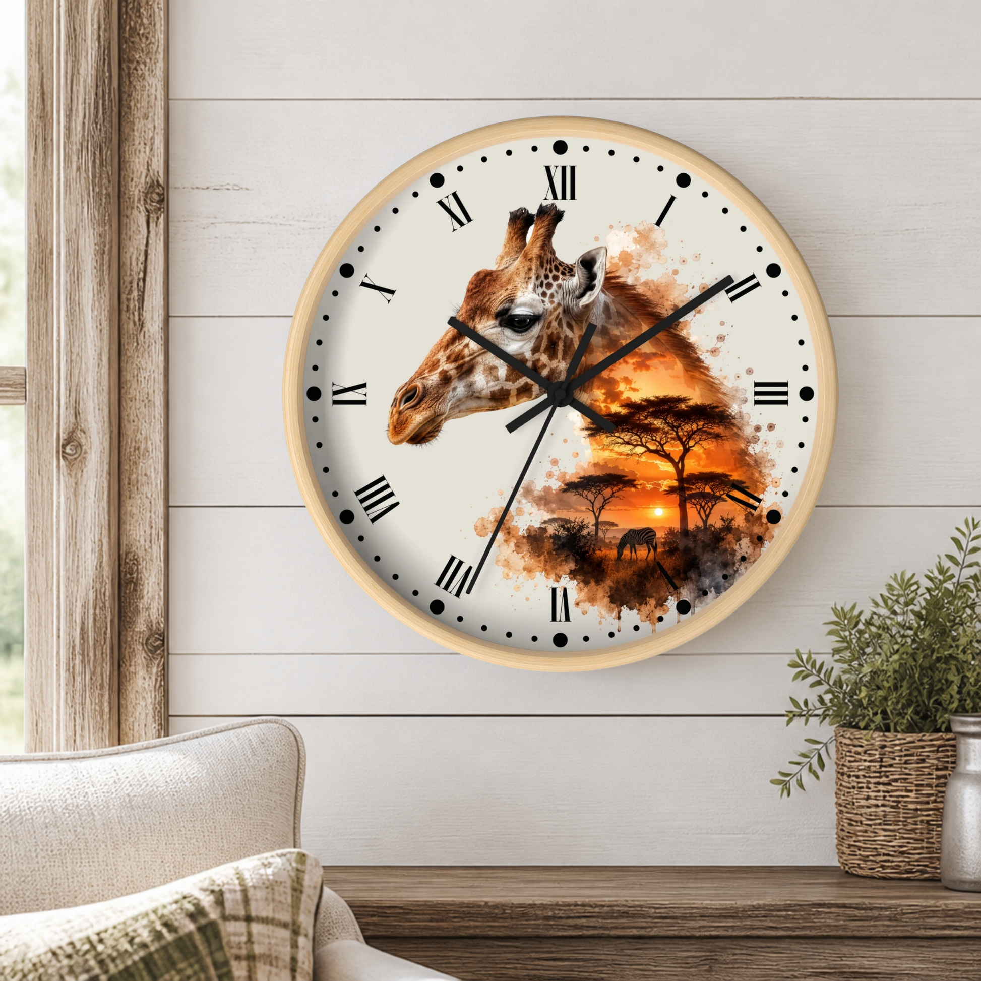 A round wall clock with a light wood frame hangs on a white shiplap wall above a wooden table. The clock face features a giraffe head and an African savanna sunset scene with acacia trees, rendered in warm orange, brown, and black tones.