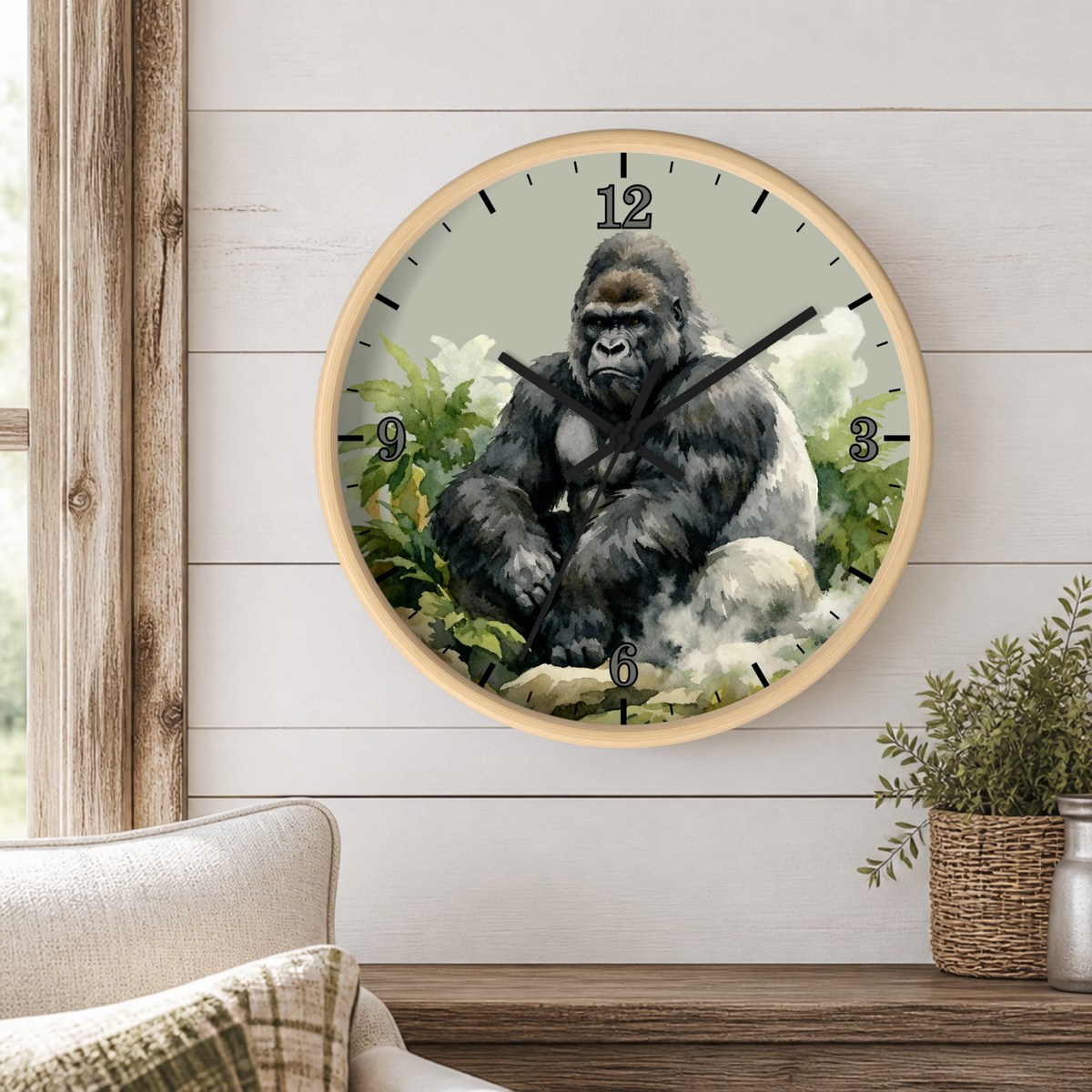 A round wall clock with a light wood frame hangs on a white shiplap wall above a wooden console table. The clock face features a detailed illustration of a gorilla sitting among green foliage, with black Arabic numerals and hands.