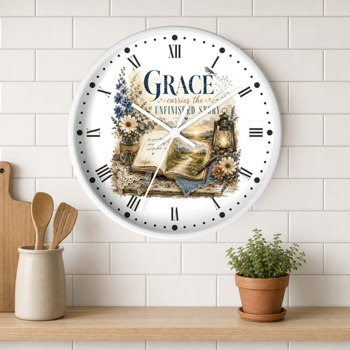 A round white wall clock with Roman numerals and a vintage-style floral illustration featuring the word 'Grace' and an open book. The clock is mounted on a white subway tile wall above a wooden shelf with a small potted plant and kitchen utensils.