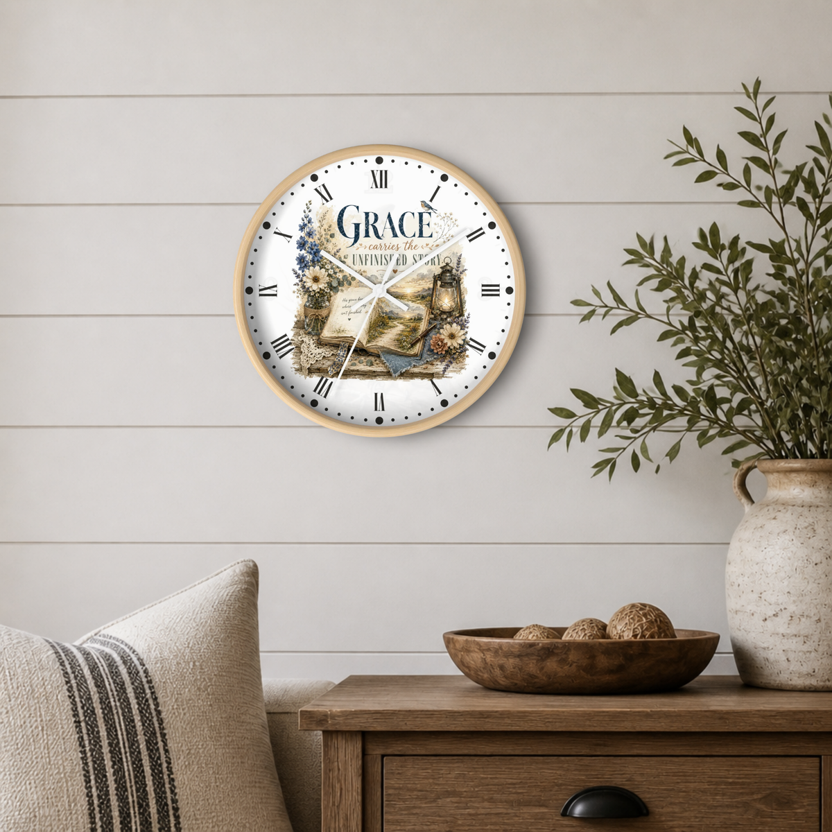 A round wall clock with a light wood frame hangs on a white shiplap wall above a wooden side table. The clock face features a vintage illustration of an open book and the words 'GRACE' and 'JESUS IS THE ONLY WAY'.