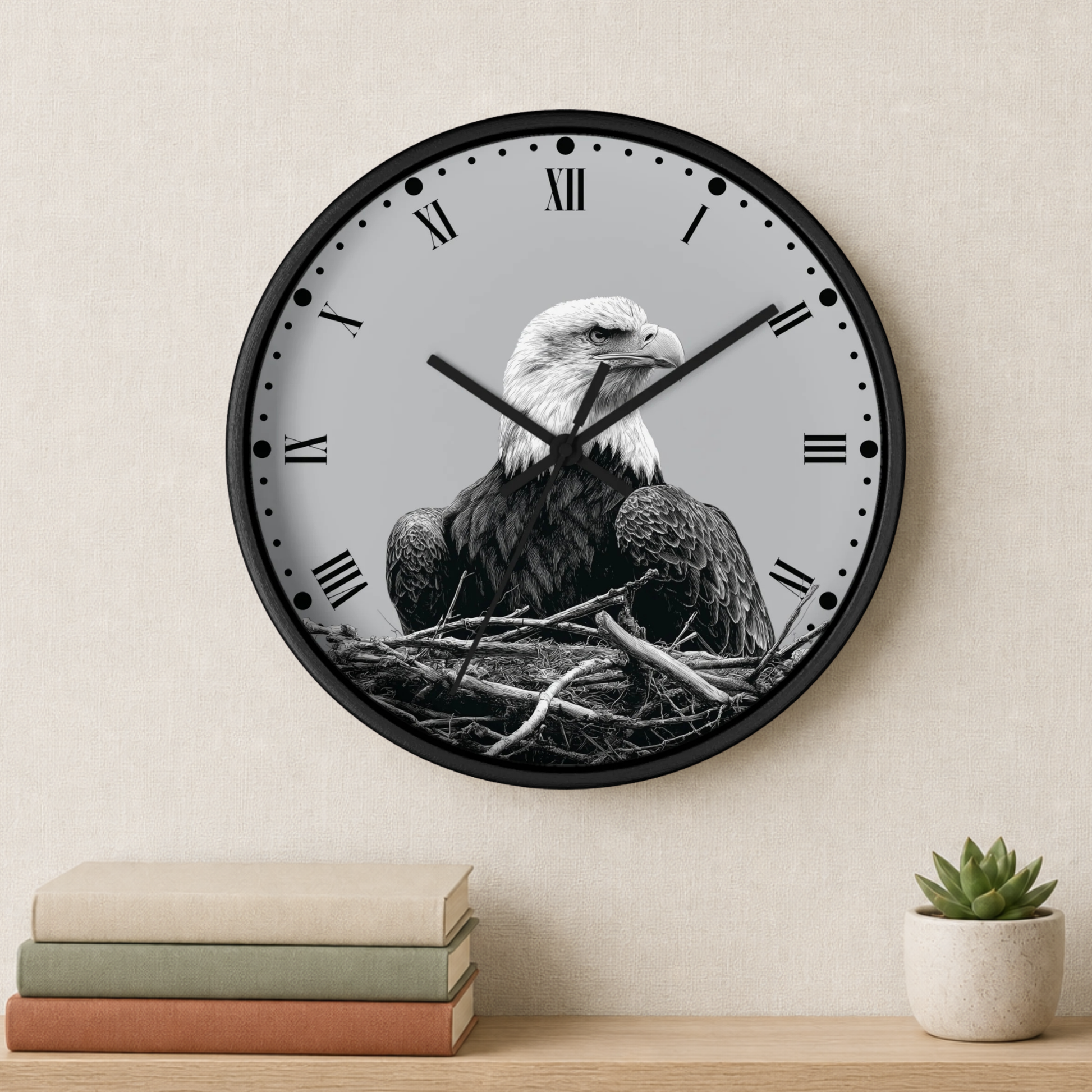 A round wall clock with a black frame and a monochrome bald eagle sitting in a nest design on the face, mounted on a beige wall above a shelf with books and a small potted succulent.