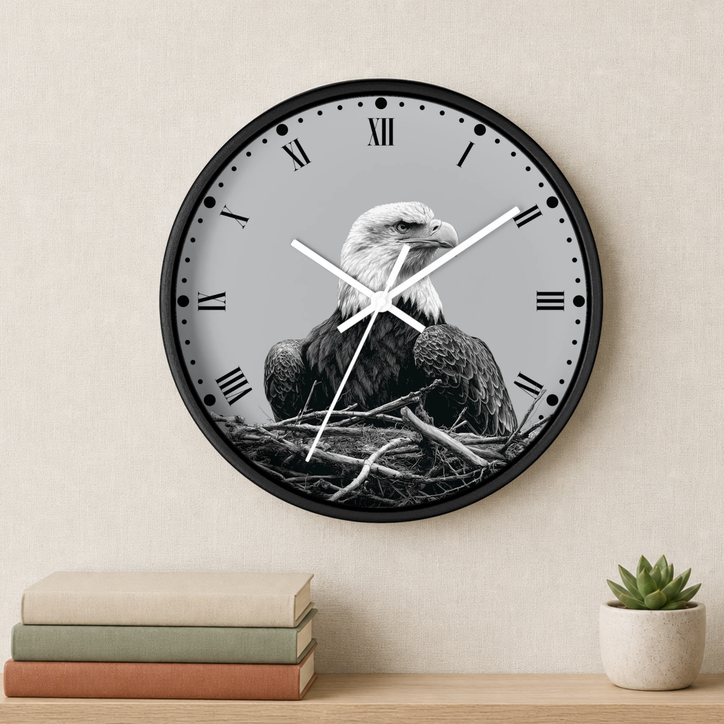 A round wall clock with a black frame and a grayscale bald eagle sitting in a nest design on the face, mounted on a beige wall above a shelf with books and a small succulent.