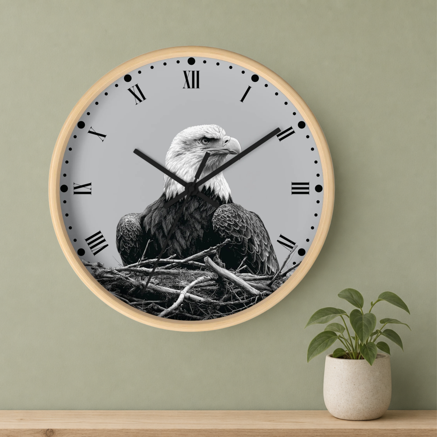 A round wall clock with a light wood frame and a black-and-white bald eagle perched in a nest design on the face, mounted on a sage green wall above a wooden shelf with a small potted plant.