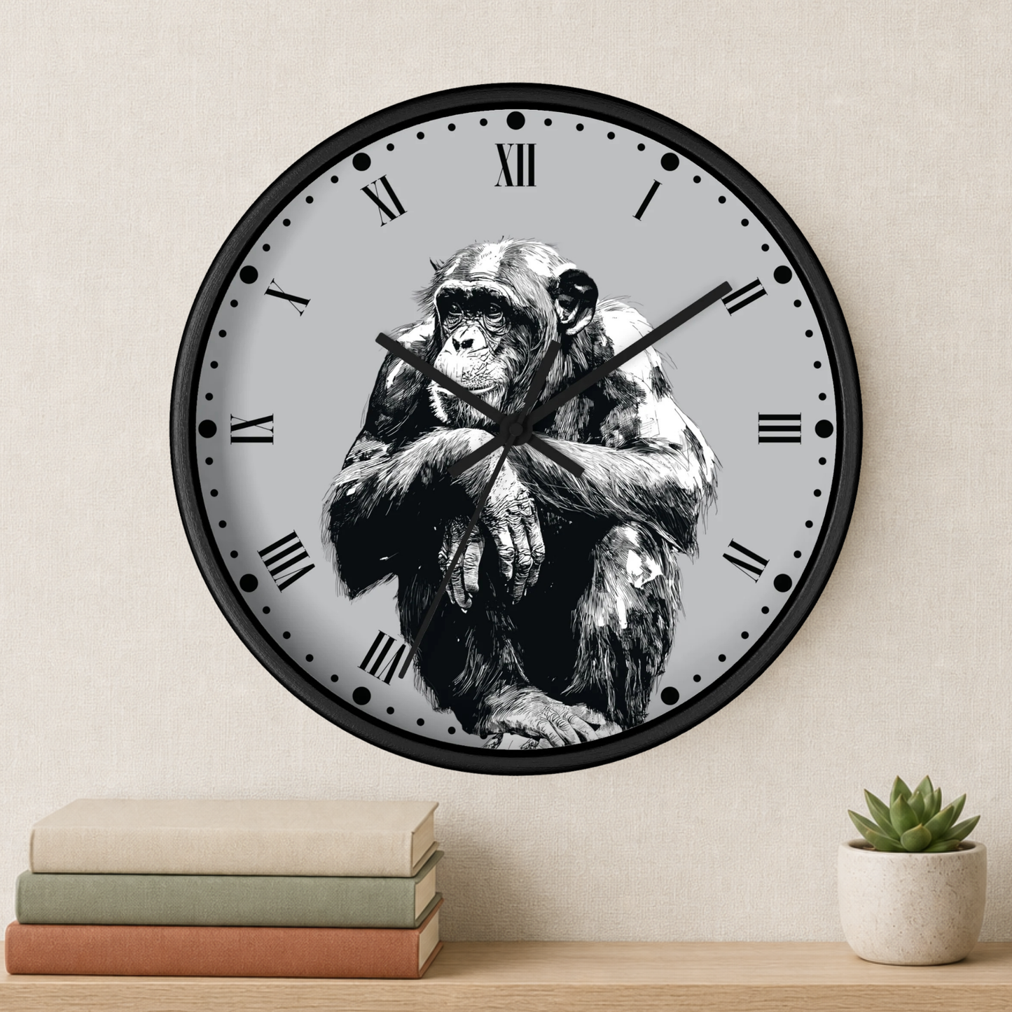 Round wall clock with a black frame and a black-and-white illustration of a chimpanzee on the clock face, styled on a beige wall above a wooden shelf with books and a small succulent.