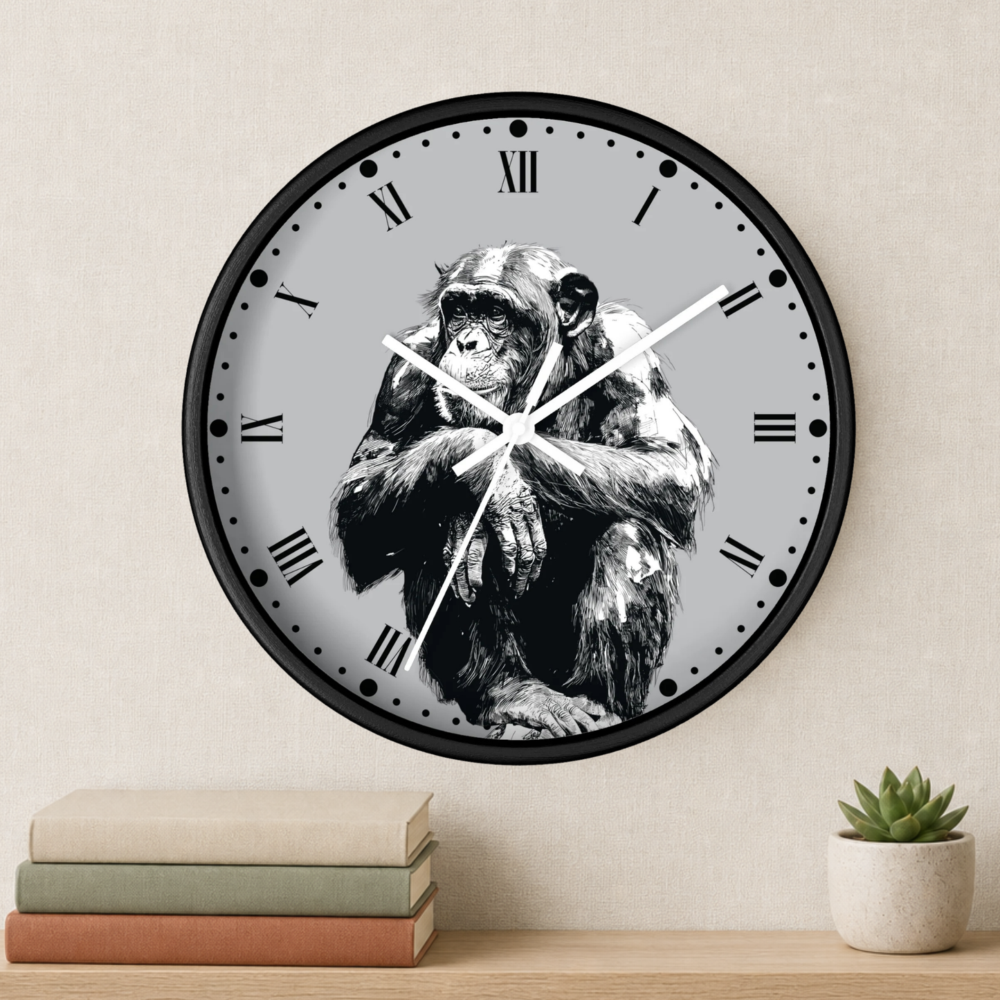 A round wall clock with a black frame and a light gray face featuring a black-and-white illustration of a chimpanzee. The clock is mounted on a beige wall above a wooden shelf holding stacked books and a small potted succulent.