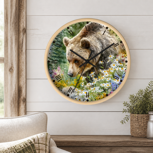 Round wall clock with a light wood frame featuring a printed design of a brown bear among wildflowers, mounted on a white shiplap wall above a wooden mantel with a small potted plant.
