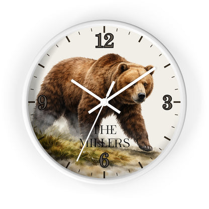A round wall clock with a white frame and a printed design featuring a brown grizzly bear walking across a grassy landscape. The clock face is off-white with black Arabic numerals and hands, and the words 'THE MILLERS' printed near the bottom.