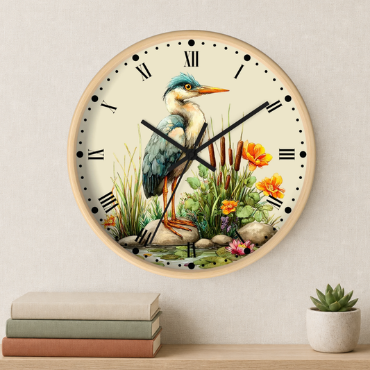 Round wall clock with a natural wood frame and a detailed illustration of a blue heron standing among grass and flowers on the clock face. The clock is mounted on a light beige textured wall above a wooden shelf with stacked books and a small potted succulent.