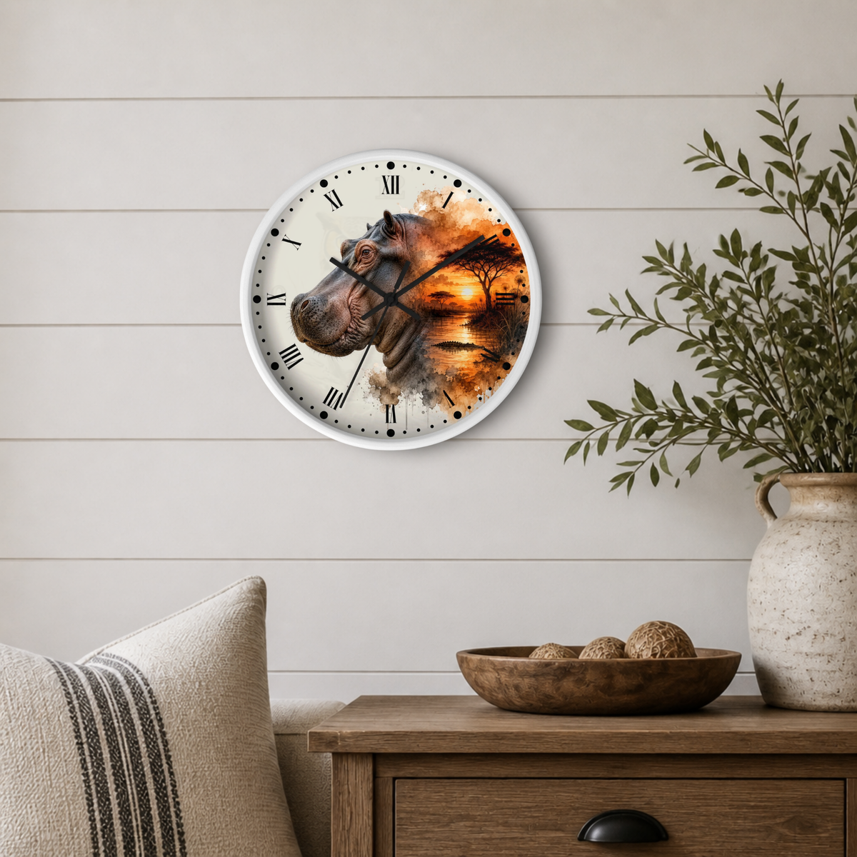 A round wall clock with a white frame hangs on a light beige shiplap wall above a wooden side table. The clock face features a surreal artistic design blending a hippopotamus head on the left with a fiery orange sunset landscape on the right.