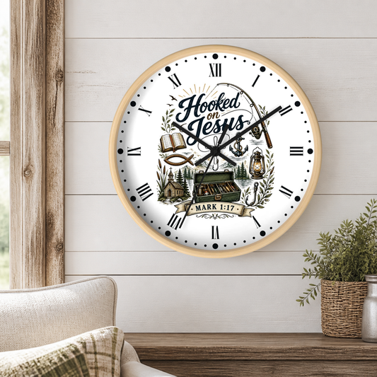 A round wall clock with a light wood frame and a white face featuring the text 'Hooked on Jesus' and 'Mark 1:27' with rustic illustrations, shown mounted on a white shiplap wall above a wooden table with a plant.