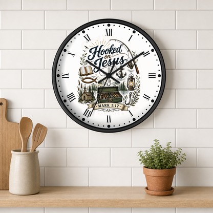 A round wall clock with a black frame and a white face featuring the text 'Hooked on Jesus' and religious illustrations, mounted on a white subway tile wall above a wooden shelf with kitchen utensils and a potted plant.