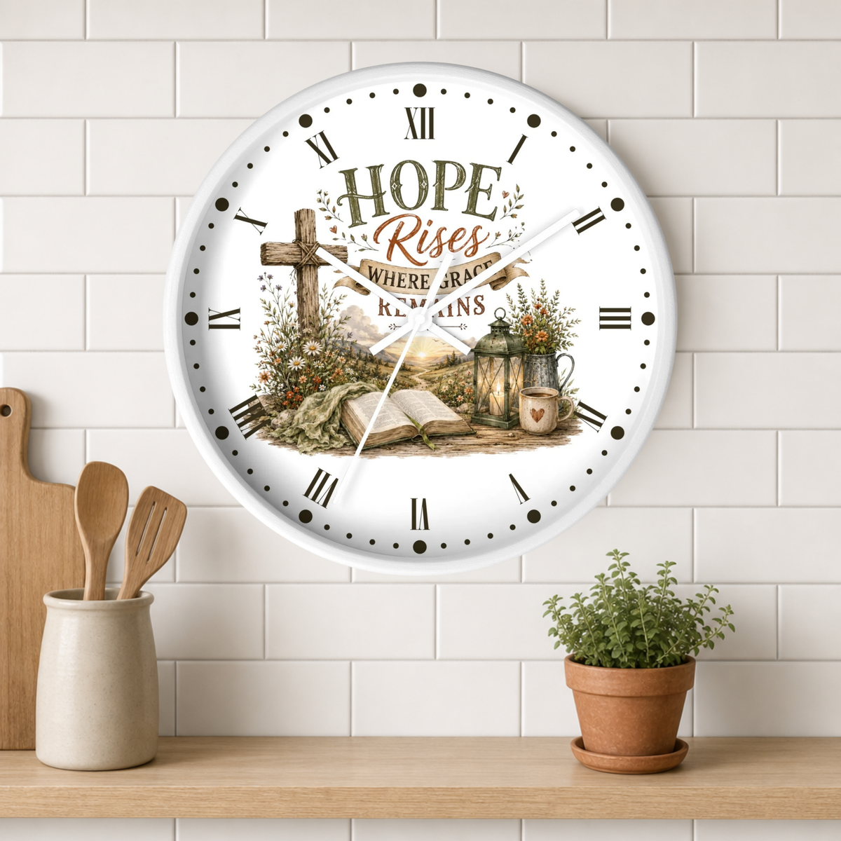 A round white wall clock with a rustic Christian-themed design featuring the words 'HOPE Rises WHERE GRACE REMAINS' around an illustration of a cross, book, lantern, and flowers. The clock is mounted on a white subway tile wall above a wooden shelf with kitchen utensils and a potted plant.