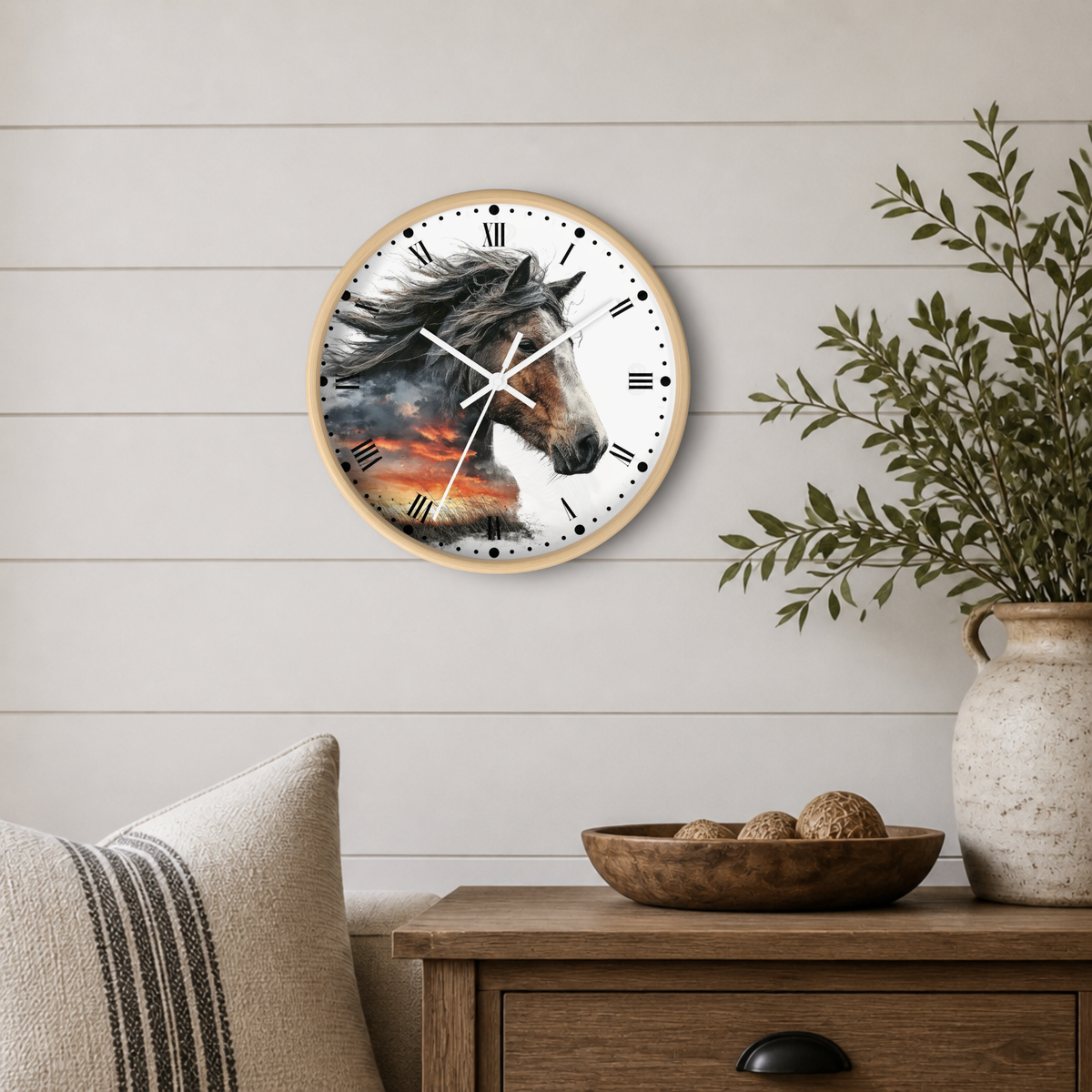 Round wall clock with a light wood frame and a printed horse portrait on the face, mounted on a white shiplap wall above a wooden side table with a plant and bowl.
