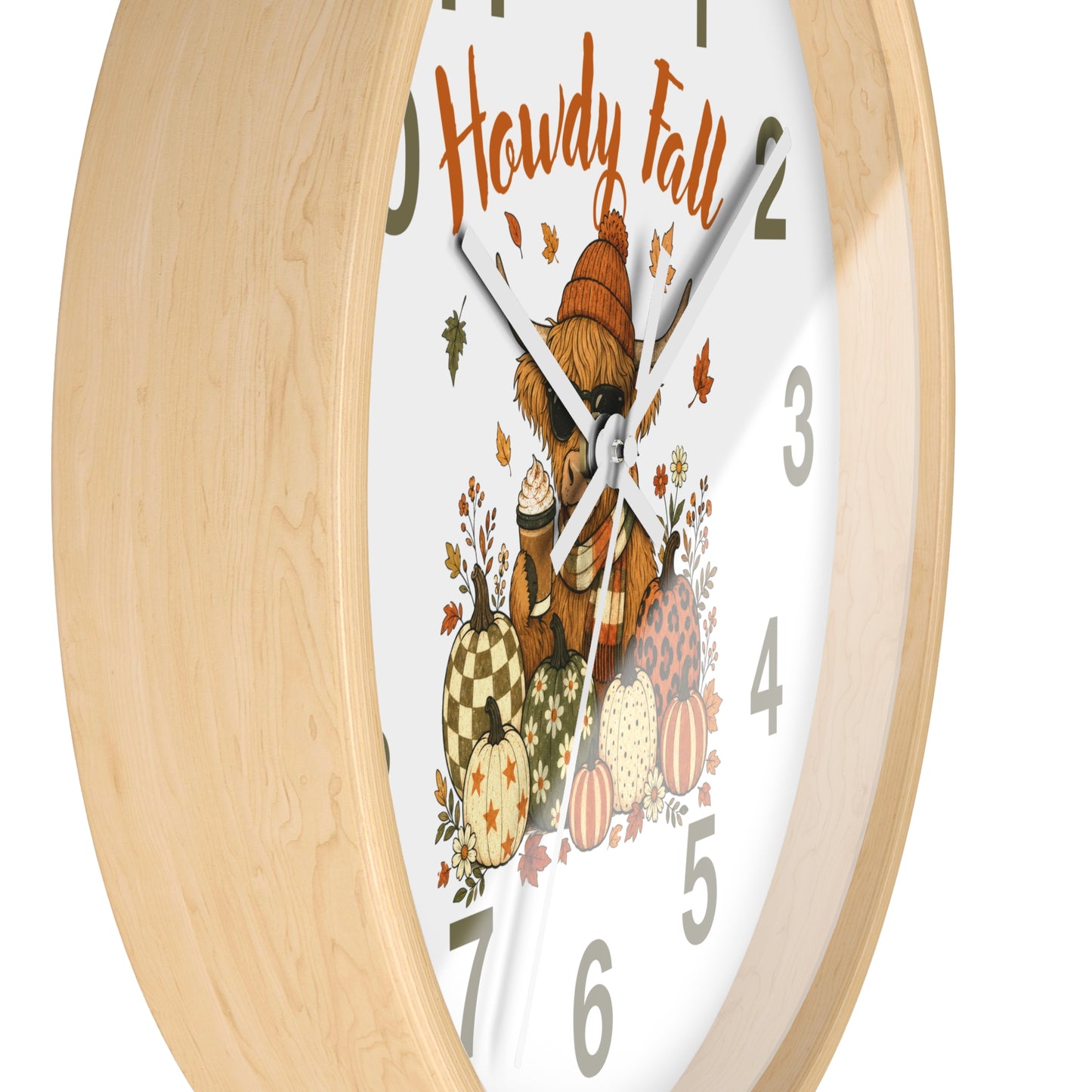A close-up of a round wall clock with a light natural wood frame and a white face featuring a cozy autumn illustration. The design includes the words 'Howdy Fall,' a bear in a hat, pumpkins, acorns, and scattered leaves, with gray Arabic numerals and silver hands.