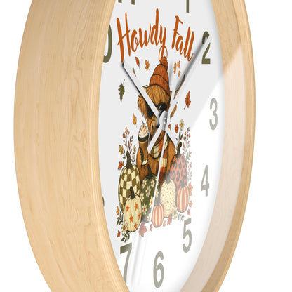 A close-up of a round wall clock with a light natural wood frame and a white face featuring a cozy autumn illustration. The design includes the words 'Howdy Fall,' a bear in a hat, pumpkins, acorns, and scattered leaves, with gray Arabic numerals and silver hands.