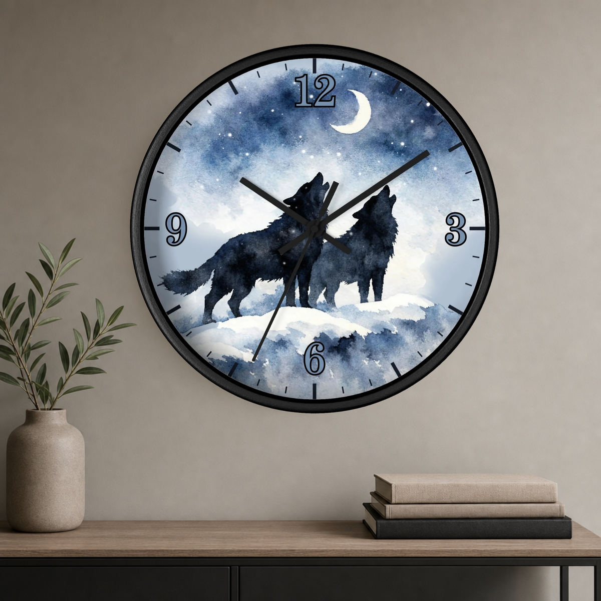 A round wall clock with a black frame hangs on a beige wall above a console table. The clock face features a watercolor-style night scene with two black howling wolves under a crescent moon and stars.