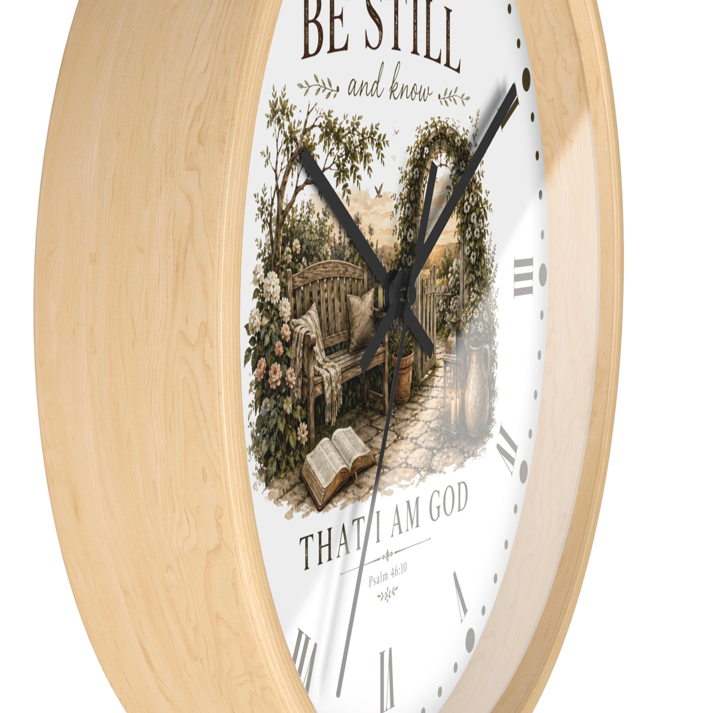A round wall clock with a light natural wood frame and a white face featuring a vintage-style illustration of a garden bench, flowers, and an open book, with the words 'BE STILL and know' and 'THAT I AM GOD' on a white background.