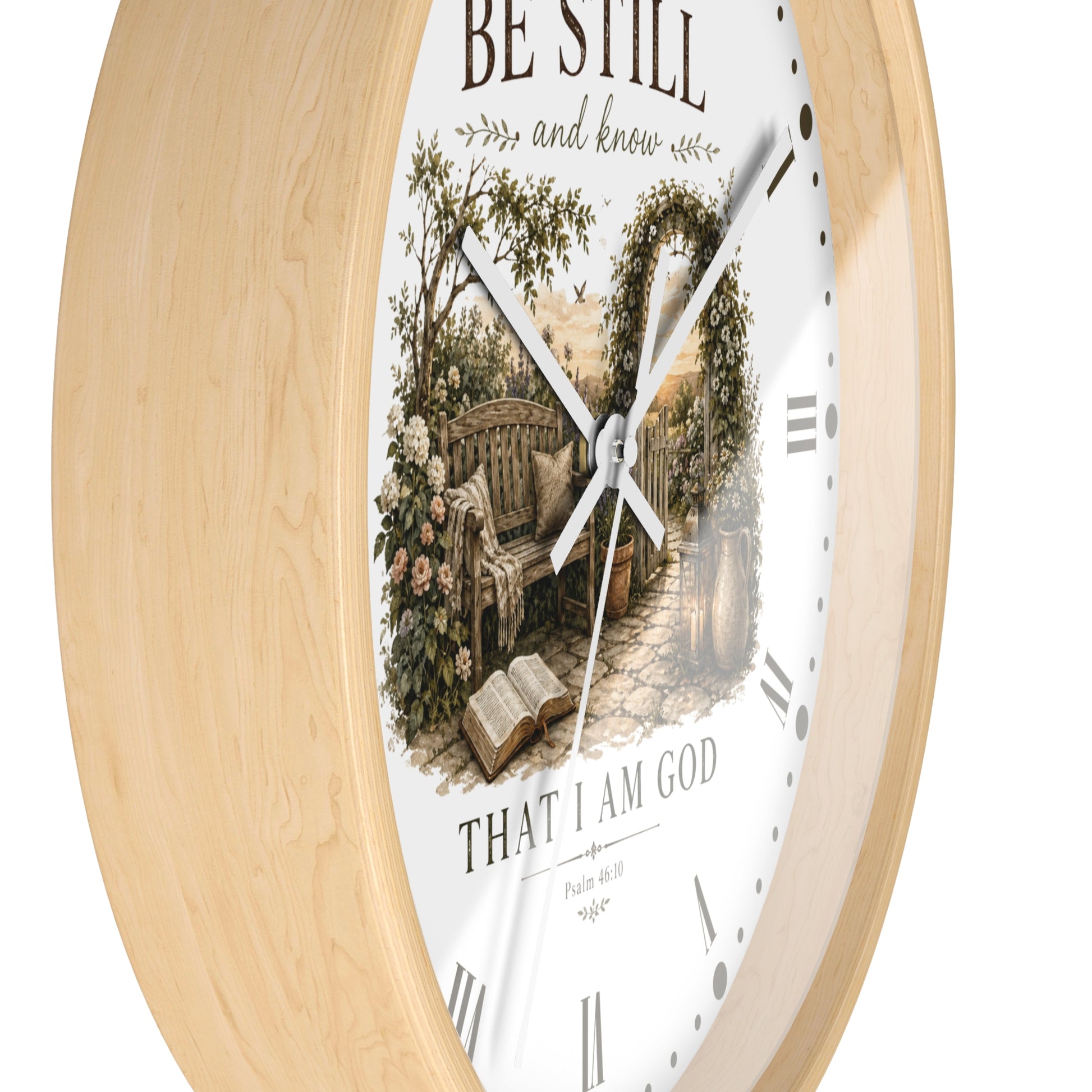 A round wall clock with a light natural wood frame and a white face featuring a vintage-style illustration of a garden bench under an arched trellis, with the text 'BE STILL and know' and 'THAT I AM GOD'.