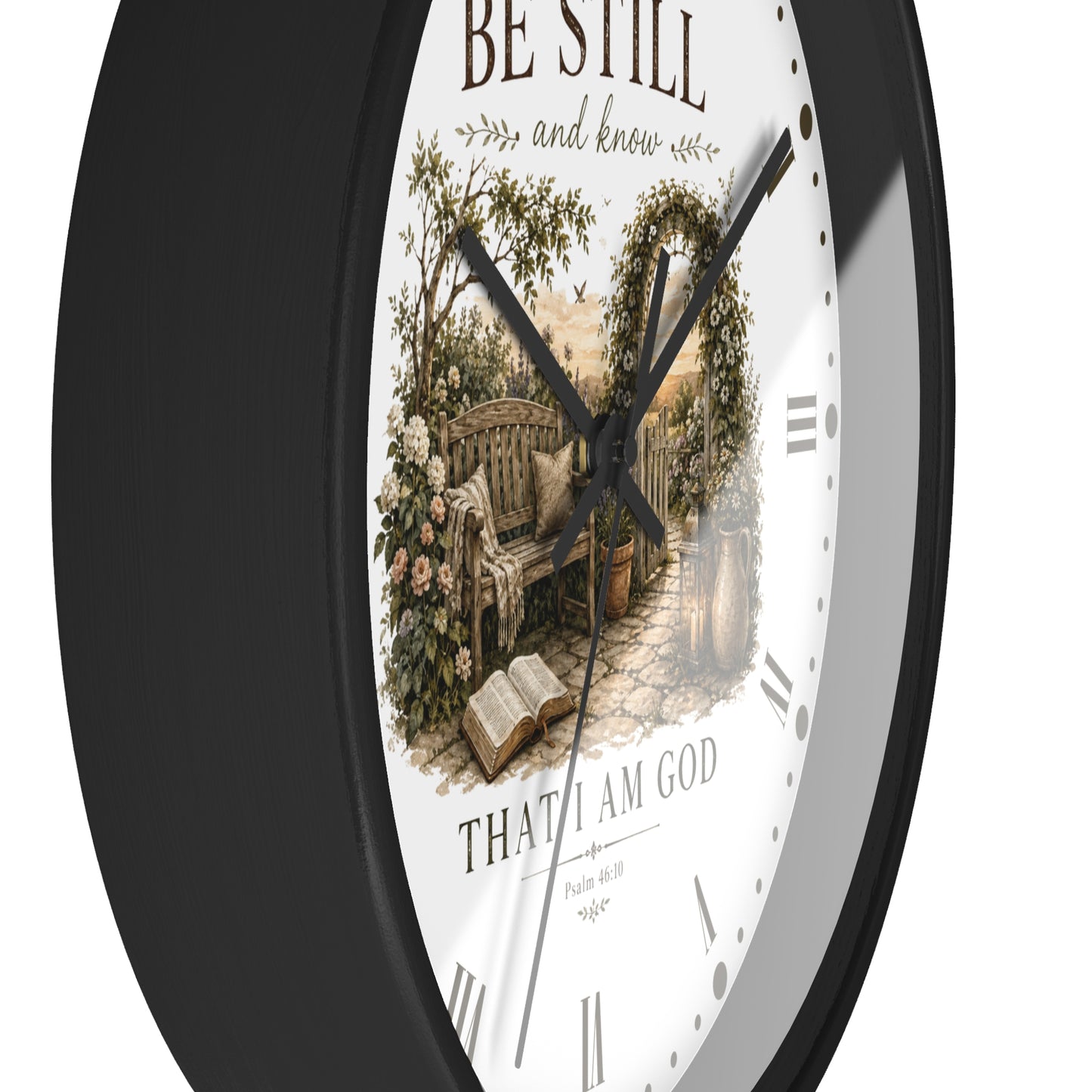 A round wall clock with a black frame and a white face featuring a vintage-style illustration of a garden bench, flowers, and an open book, with the text 'BE STILL and know' and 'THAT I AM GOD' on the dial.