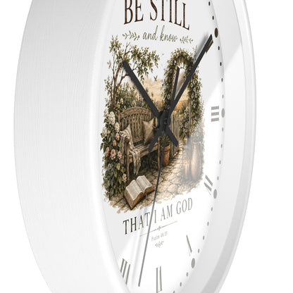 White round wall clock with a vintage-style garden bench illustration in the center and the words 'BE STILL and know' and 'THAT I AM GOD' on the dial.