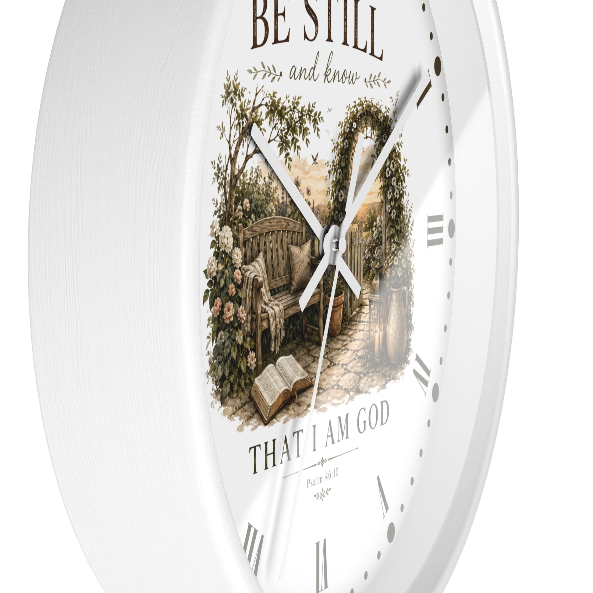 A white round wall clock with a vintage-style printed illustration of a garden bench under an arched trellis and the words 'BE STILL and know' and 'THAT I AM GOD' on the dial.