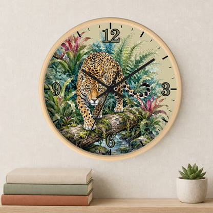 A round wall clock with a light wood frame hangs on a beige wall above a shelf with stacked books and a small potted succulent. The clock face features a detailed illustration of a leopard walking through lush green tropical foliage at night, with black Arabic numerals and black clock hands.